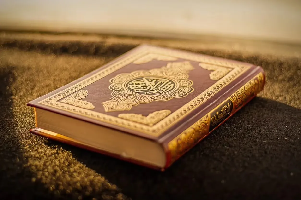 A gold-embossed Quran rests on a textured black surface, illuminated by warm, soft golden sunlight.