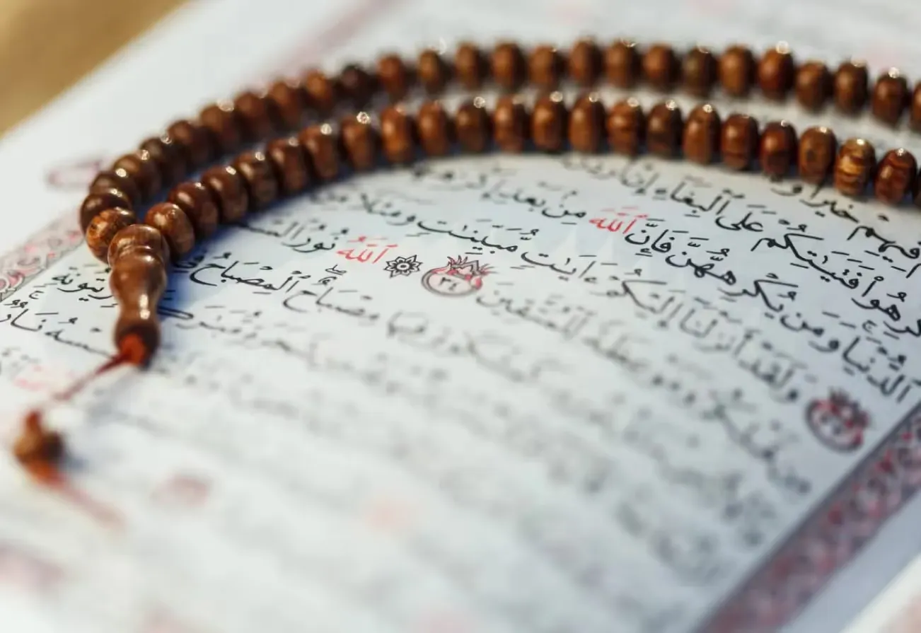 Wooden prayer beads resting on an open Quran with Arabic calligraphy during Ramadan or daily prayer.