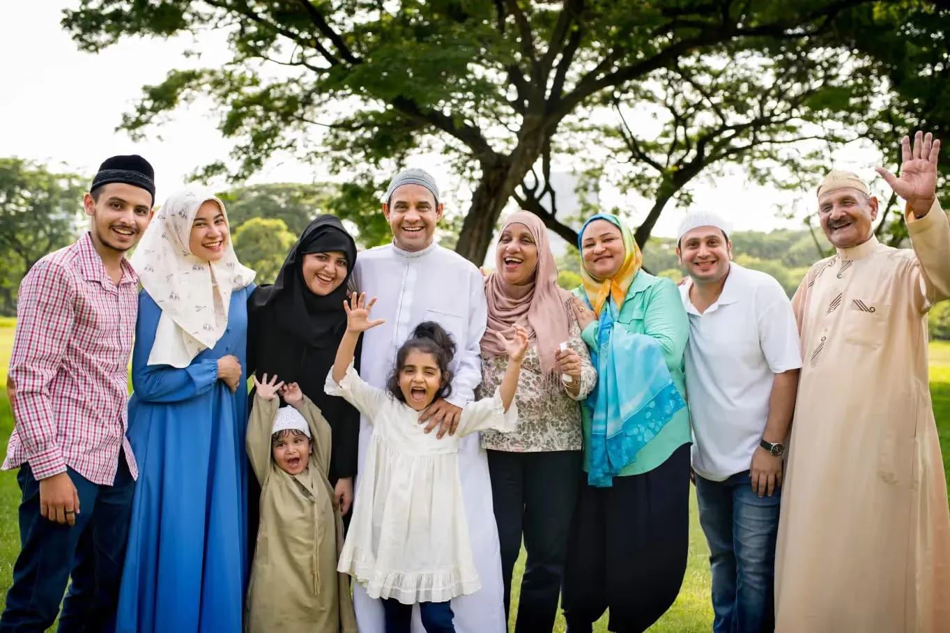 Large happy multi-generational Muslim family smiling and posing together outdoors in a park during Eid celebrations.
