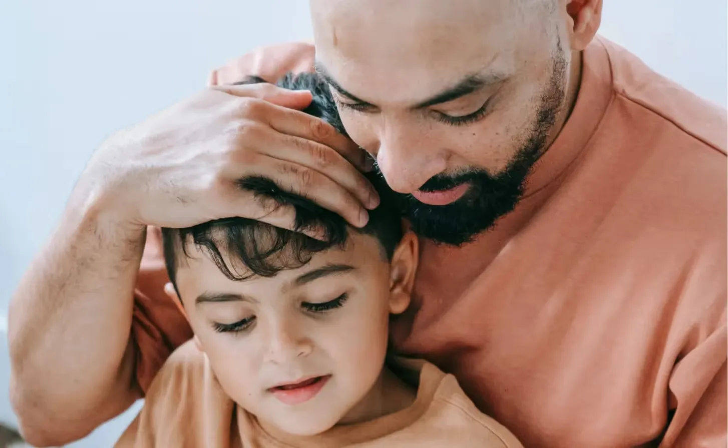 A loving father with a beard tenderly comforting and embracing his young son at home.