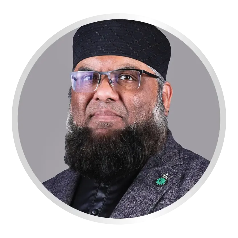 A middle-aged man with a full beard and a black patterned kufi cap wears glasses and a grey textured blazer with a small green circular lapel pin. He is positioned against a plain grey background within a circular frame.