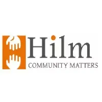 Logo for Hilm Community Matters, featuring an orange square with two white hands reaching toward each other next to the grey text "Hilm" with an orange dot over the "i" and the tagline "COMMUNITY MATTERS" underneath.