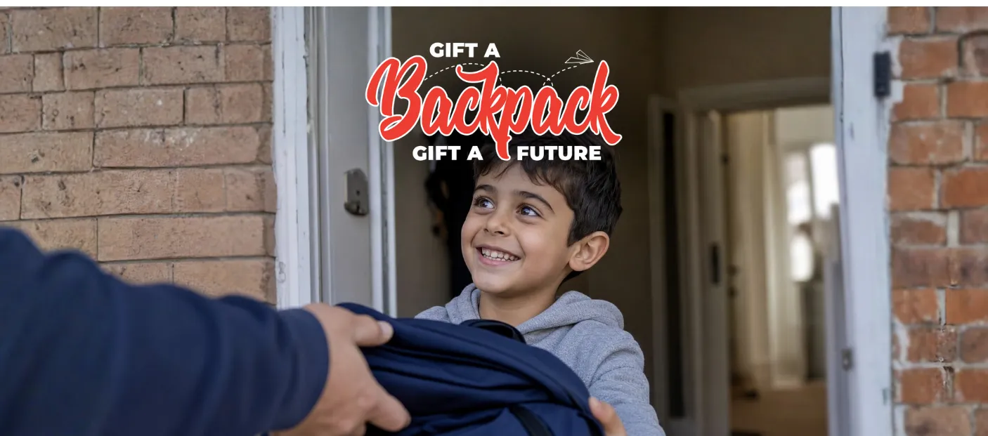 A smiling boy holds a backpack, showcasing a cheerful expression and a sense of excitement.