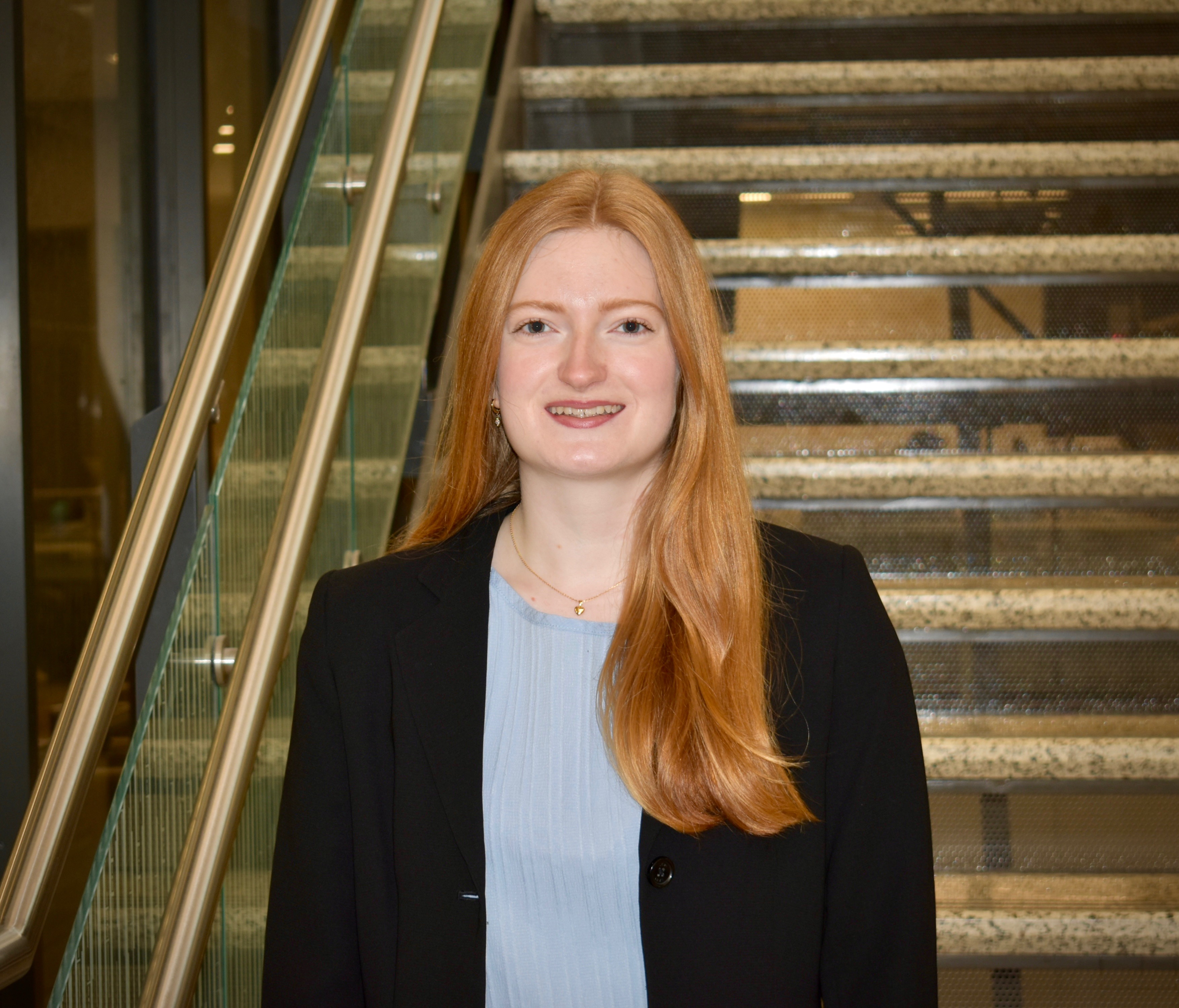 A woman with red hair in a black blazer and blue shirt.