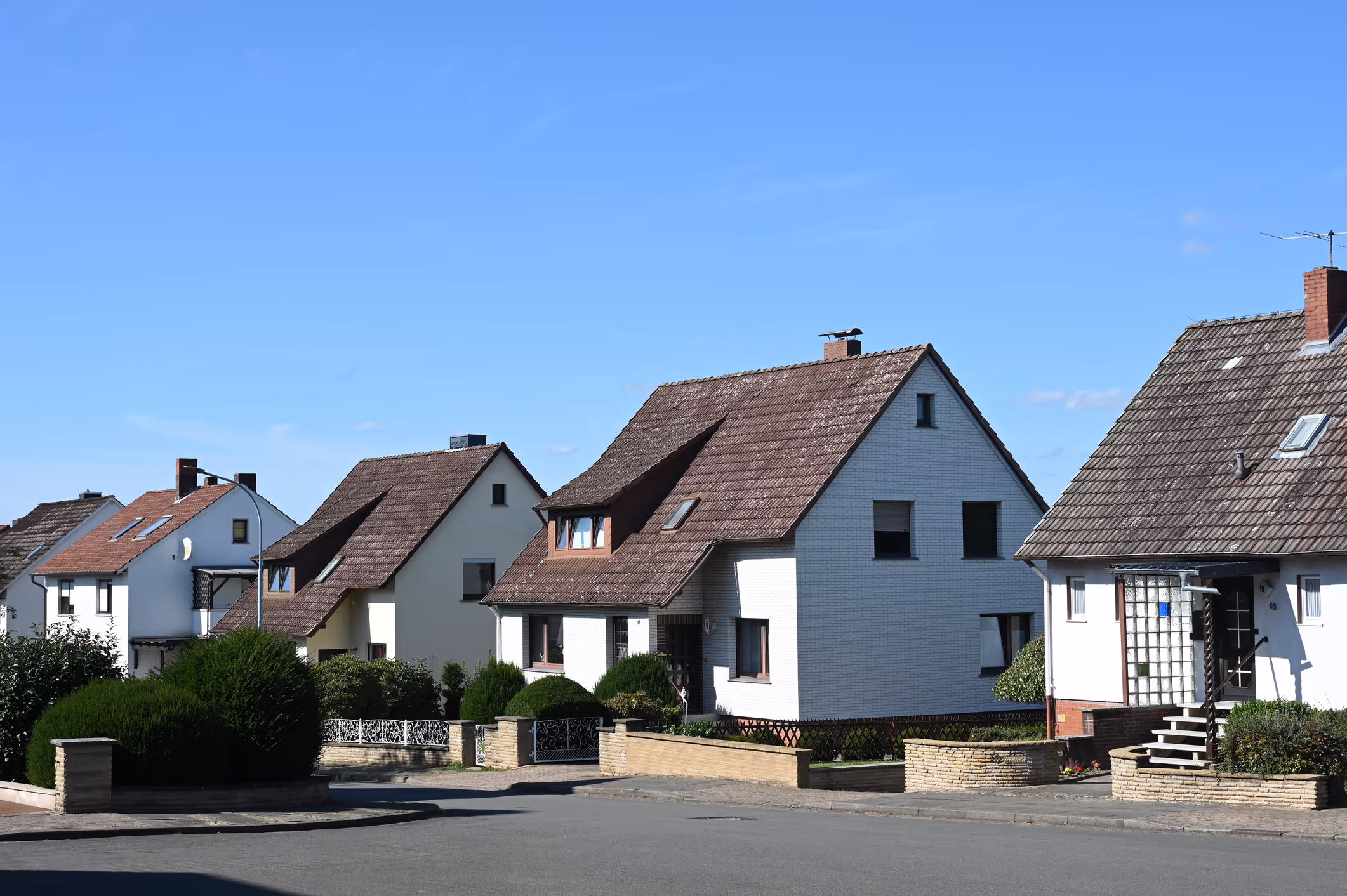 Reihe aus 4 kleinen Einfamilienhäusern der 1950er Jahre, die zu Effizienzhasu 85 saniert werden könnten, fotografiert von der gegeüberliegenden Straßenseite