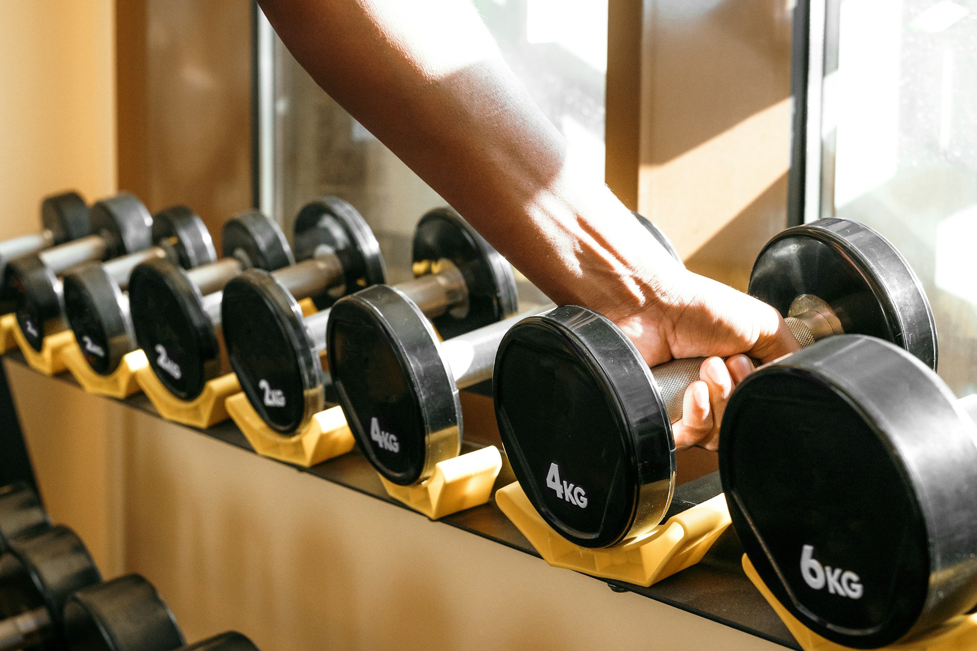 Eine linke Männerhand greift eine Kurzhantel im Fitnesstudio von der Gewichtsablage