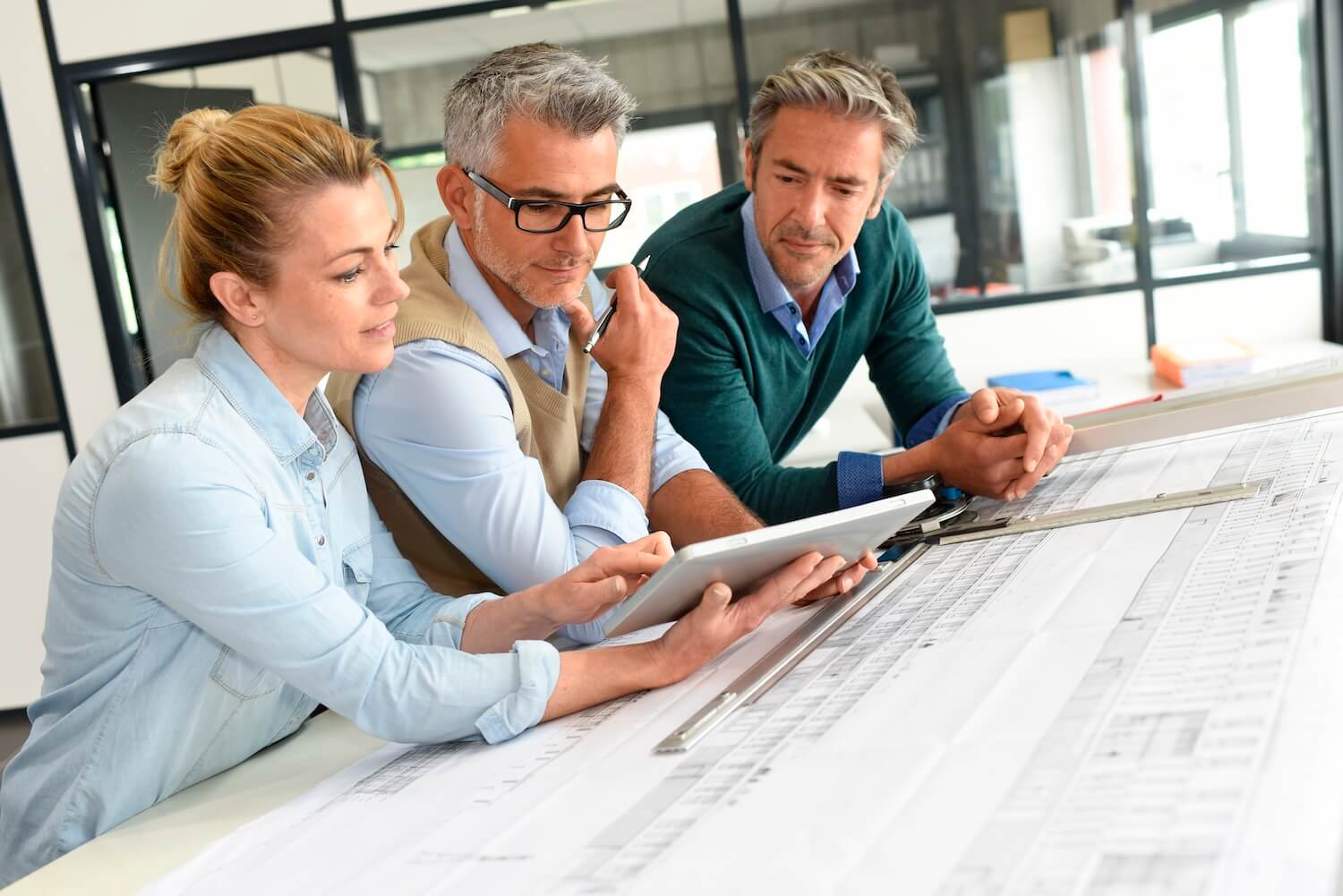 Architektenteam prüft Baupläne auf Tablet – Wie lange dauert eine Baugenehmigung im Planungsbüro?