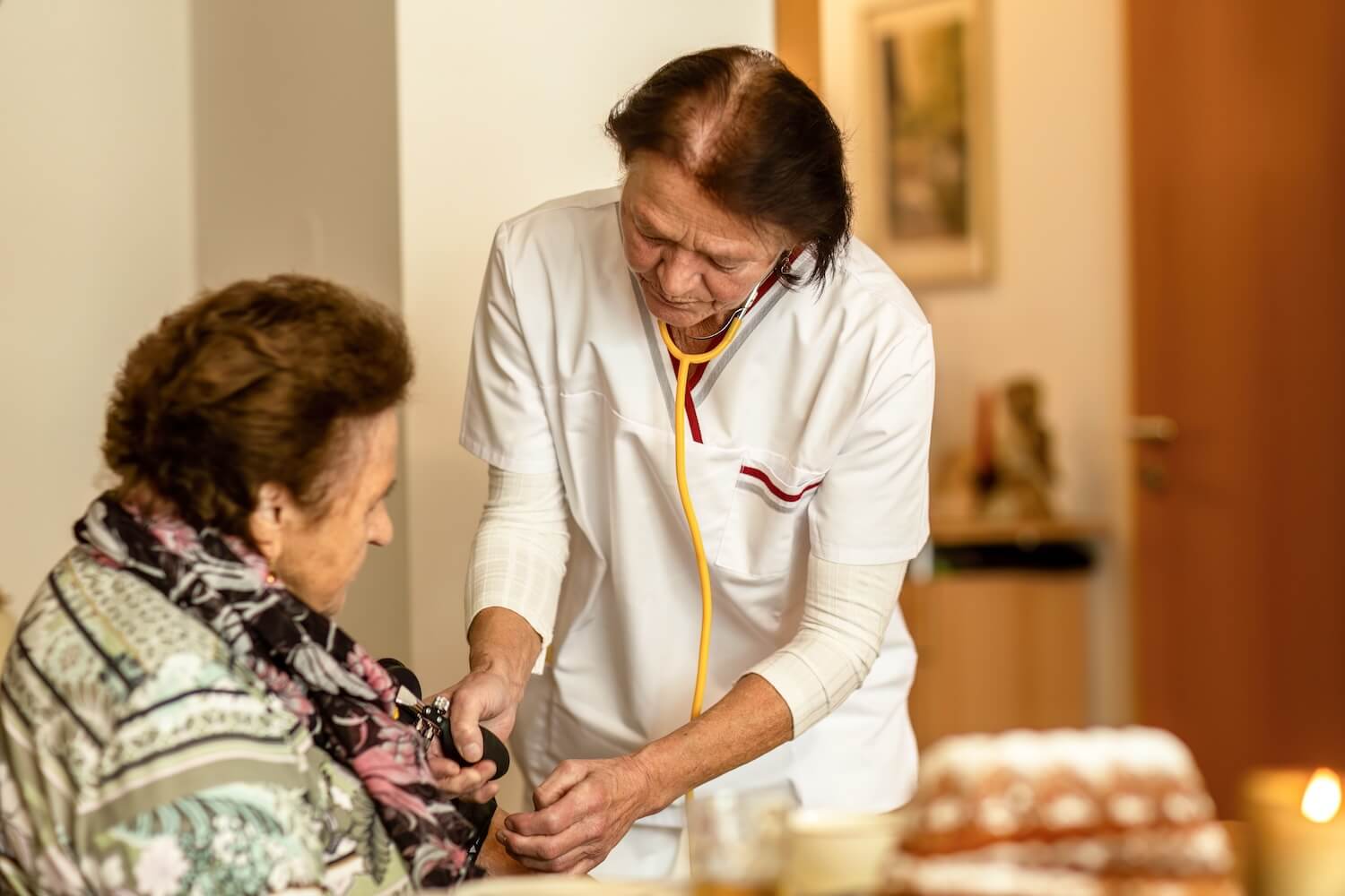 Pflegerin misst Blutdruck bei Seniorin im häuslichen Umfeld als Beispiel für Leistungen im Rahmen einer Nutzungsänderung ambulanter Pflegedienst.