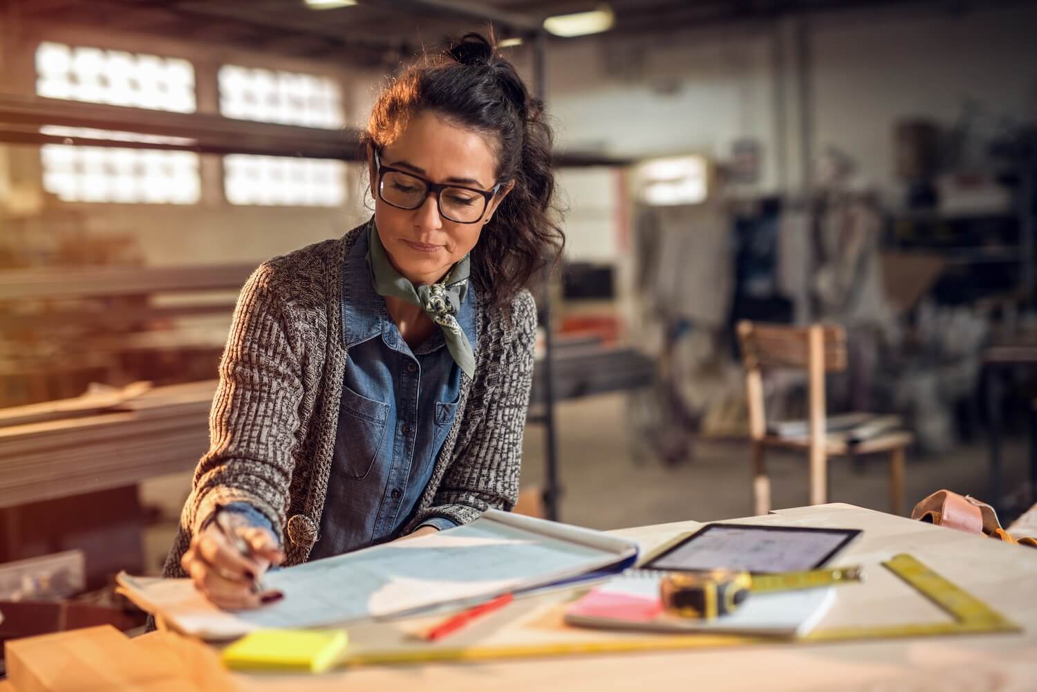 Planerin prüft Bauzeichnungen auf einem Arbeitstisch – Situation, in der ein Statiker bei Umbau- oder Sanierungsmaßnahmen hinzugezogen wird.
