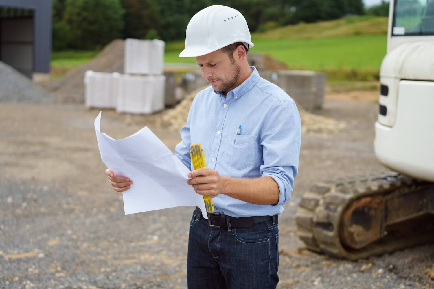Statiker mit Schutzhelm kontrolliert Baupläne auf einer Baustelle – erforderlich bei Neubauten und tragenden Konstruktionen.