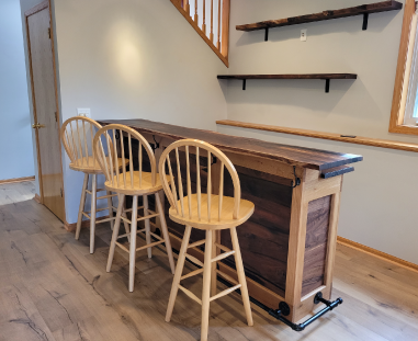A walnut bar top with matching floating shelves and three bar stools.