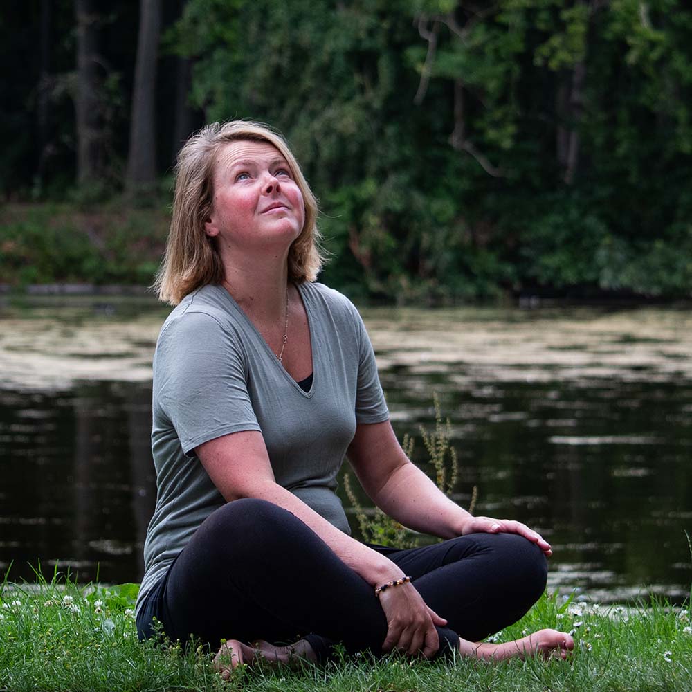 Vrouw zit aan de waterrand en kijkt omhoog