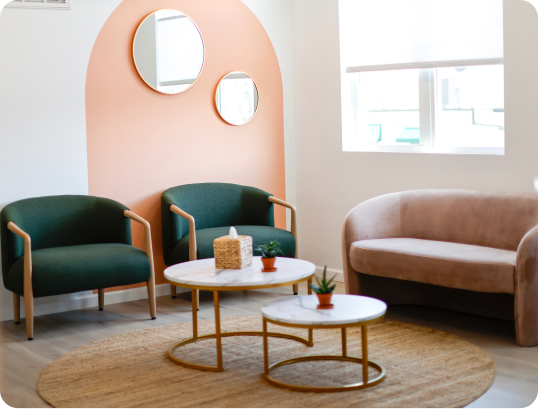 Modern living room with two green armchairs, beige sofa, round tables, and two round wall mirrors.