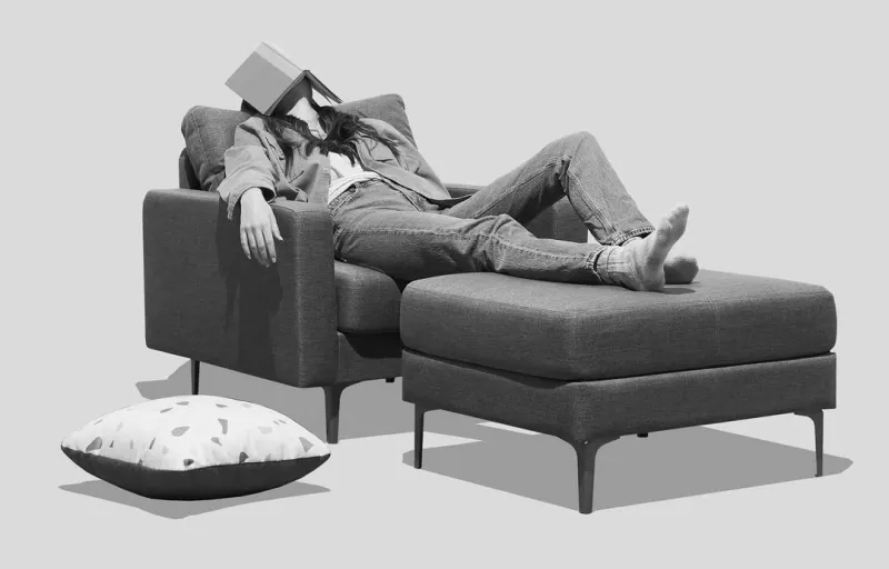 A person laying in a chair with a book on their head.