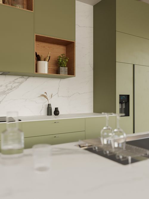 Green kitchen cabinets from the Rebel Kitchen collection, featuring shelves and decor, with a kitchen island in the foreground.