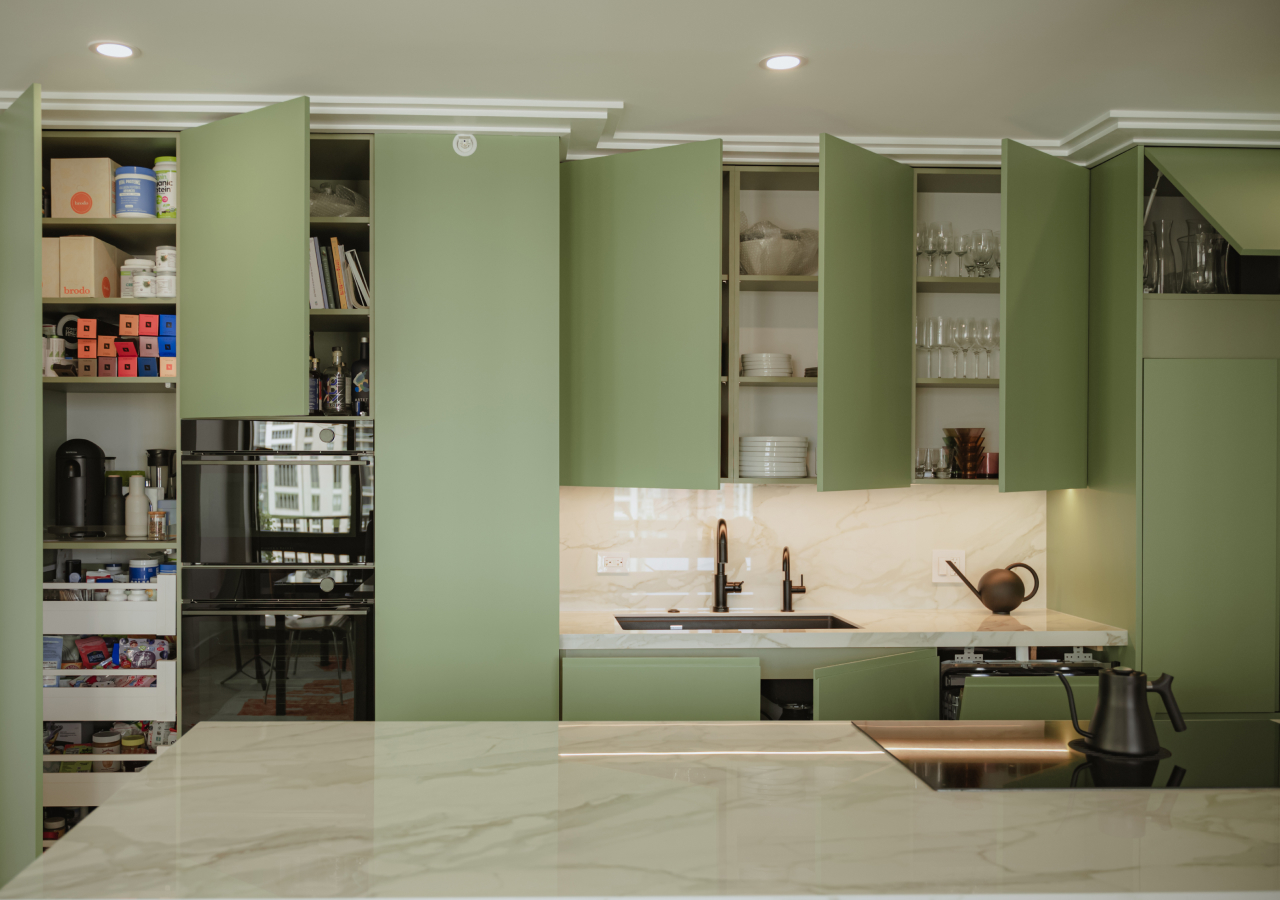 Modern minimalist kitchen with matte green cabinets, marble backsplash and countertops, black fixtures, and open shelving revealing organized storage and glassware.