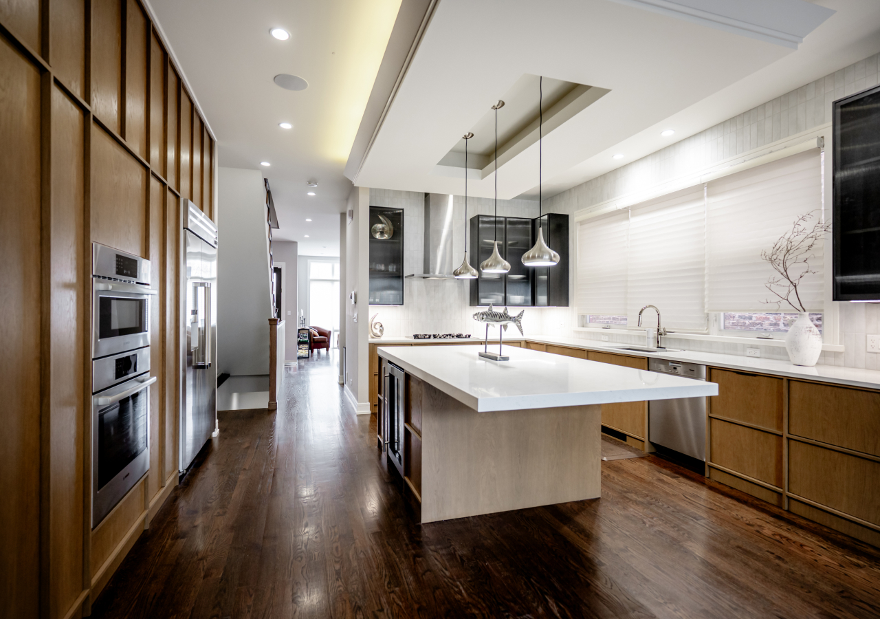 Modern Japandi kitchen with light oak cabinets, white island, stainless steel appliances, and pendant lights over dark hardwood flooring.