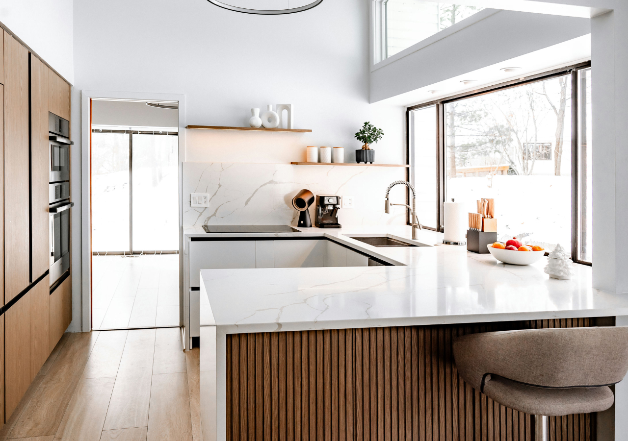 Modern kitchen with fluted wood island, white marble countertops, minimalist cabinetry, and large windows filling the space with natural light.