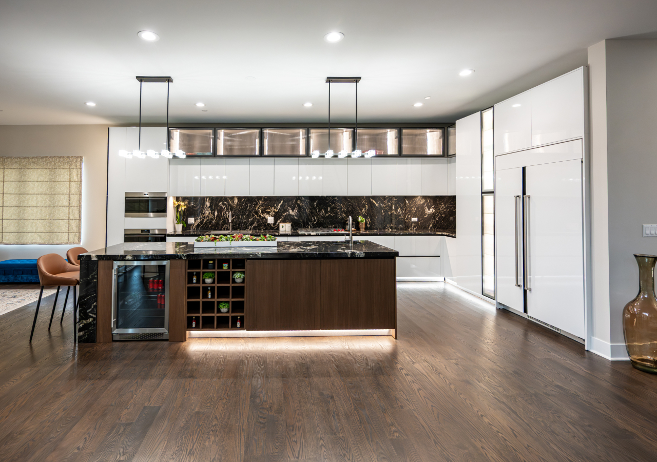 Contemporary kitchen with glossy white cabinets, a large island with dark marble surfaces, wood accents, built-in storage, and sleek pendant lighting.