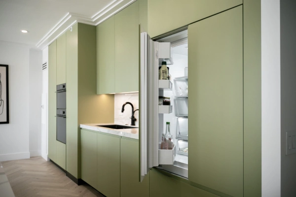 Sage green kitchen with a tall cabinet open to a built-in fridge