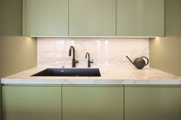 Sage green cabinets with a marble backsplash and a black faucet