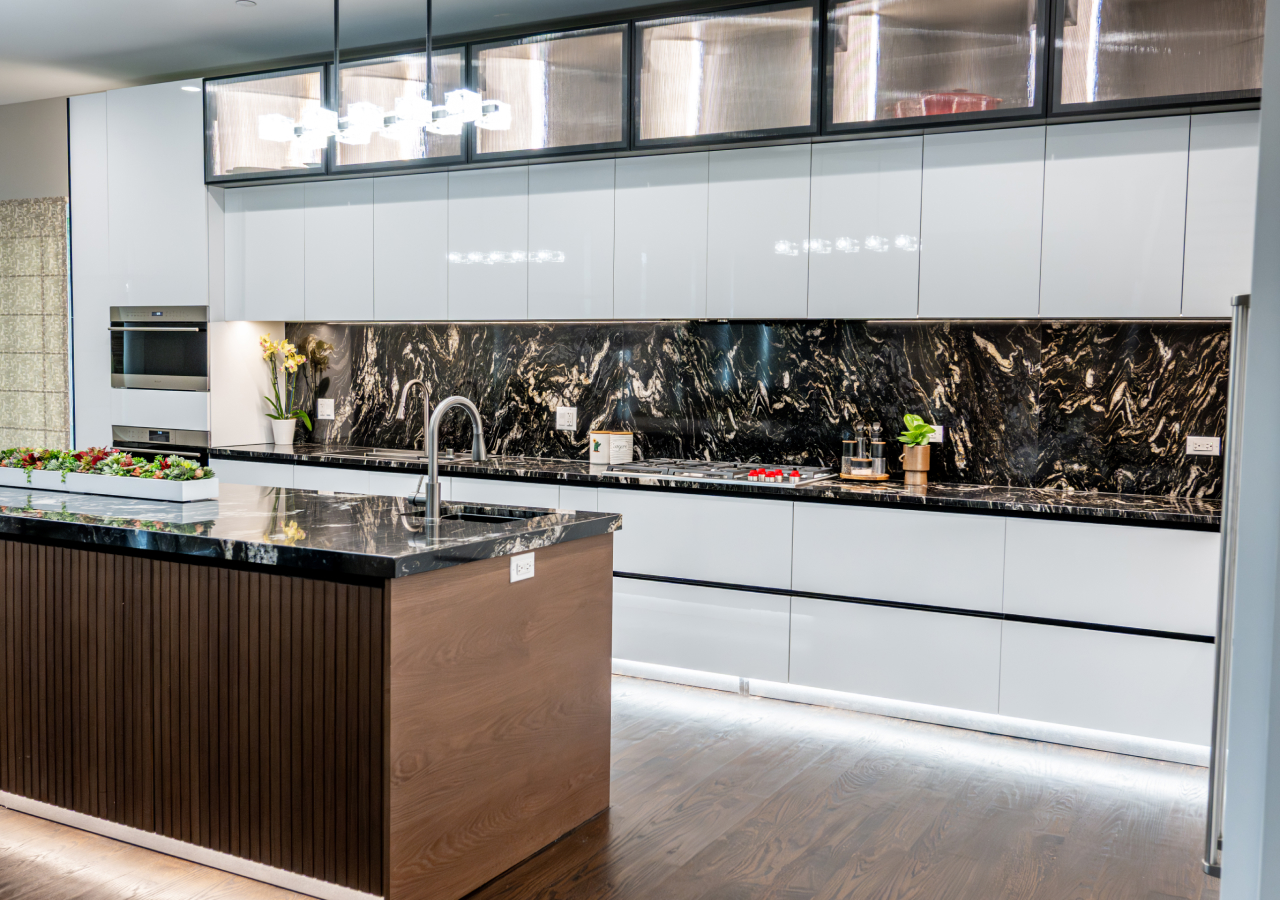 Grey kitchen with a black marble backsplash and lit upper cabinets
