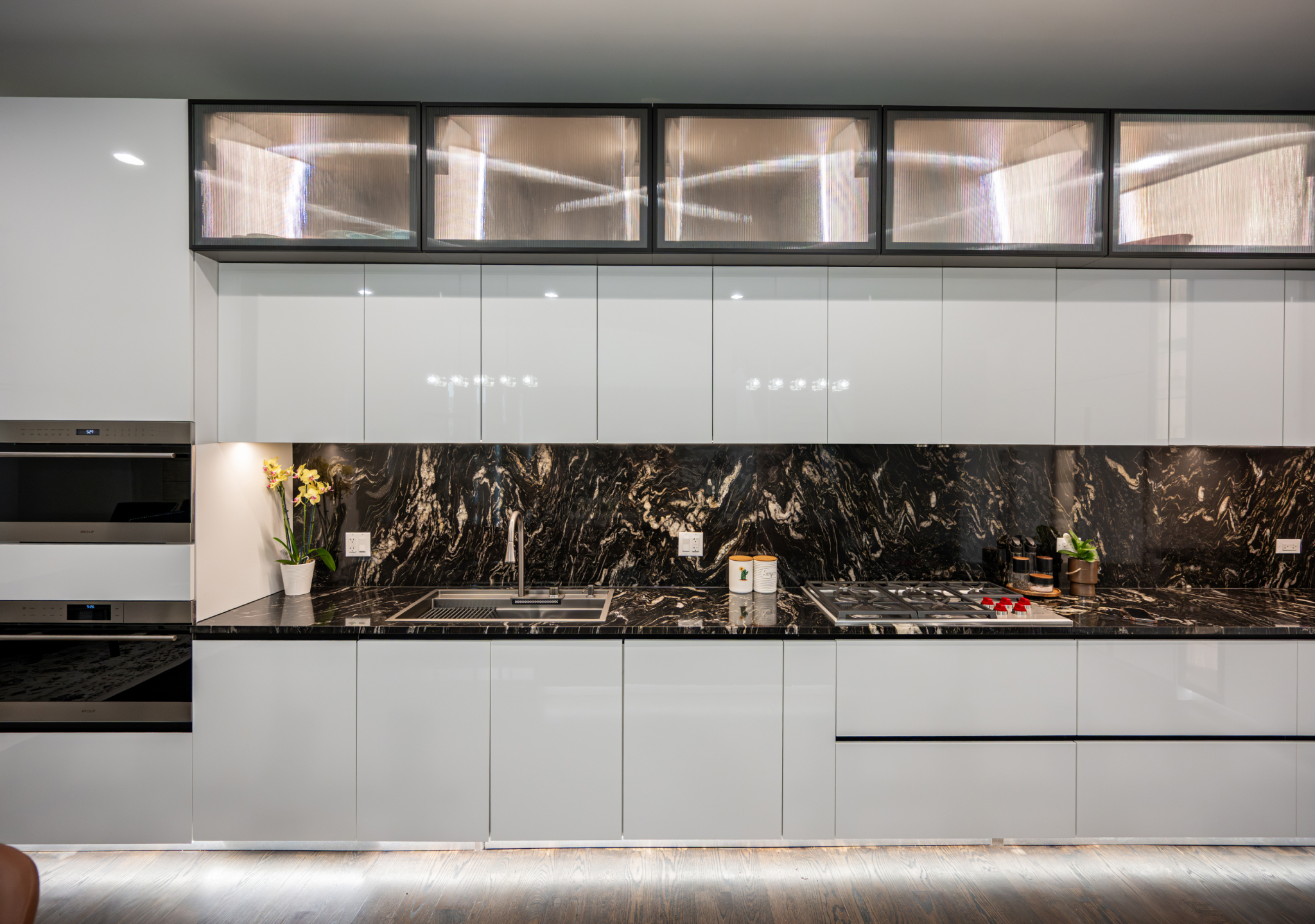 White kitchen with a black marble backsplash and lit upper cabinets