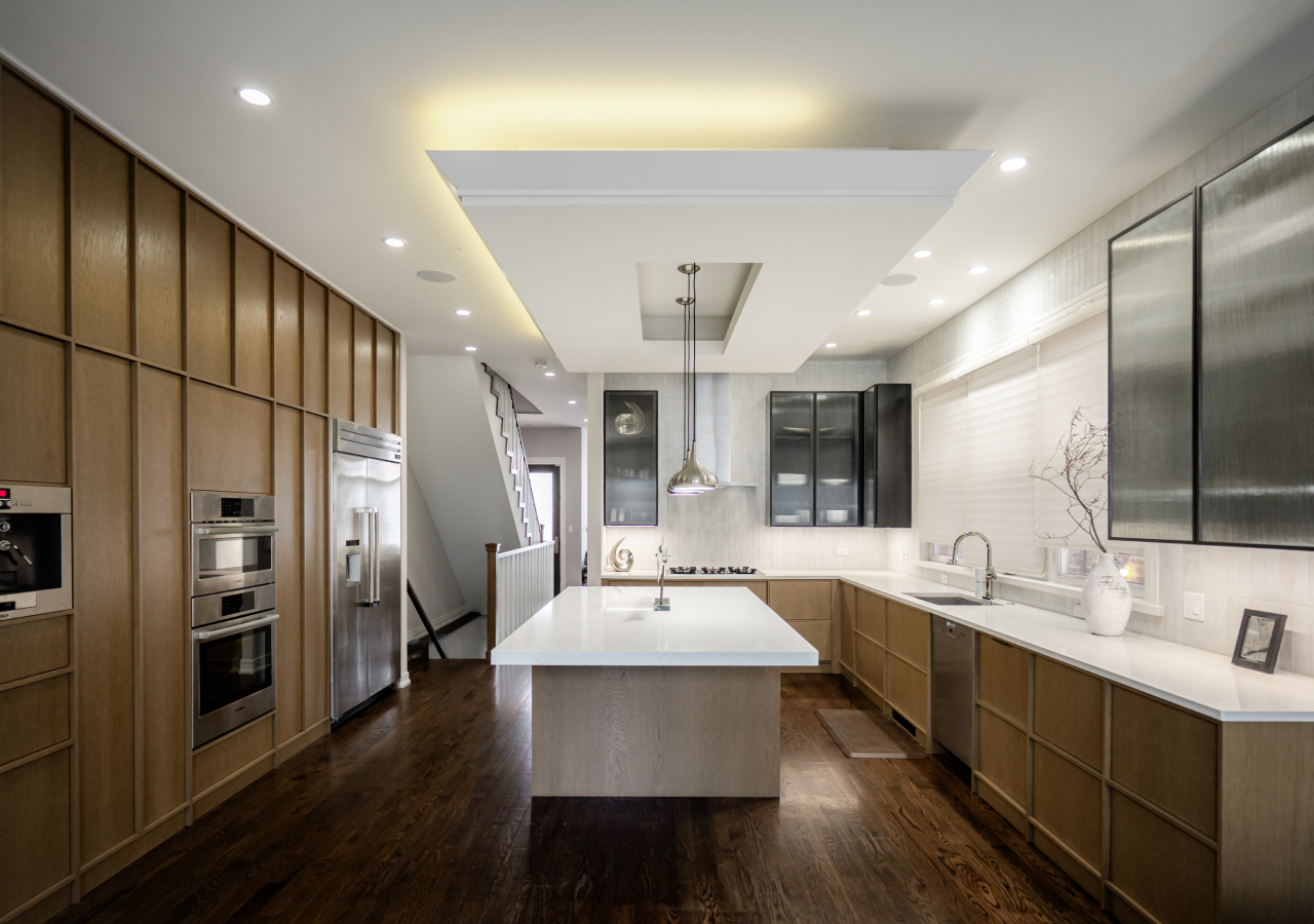 Walnut kitchen with a white island in a long room with a lit ceiling