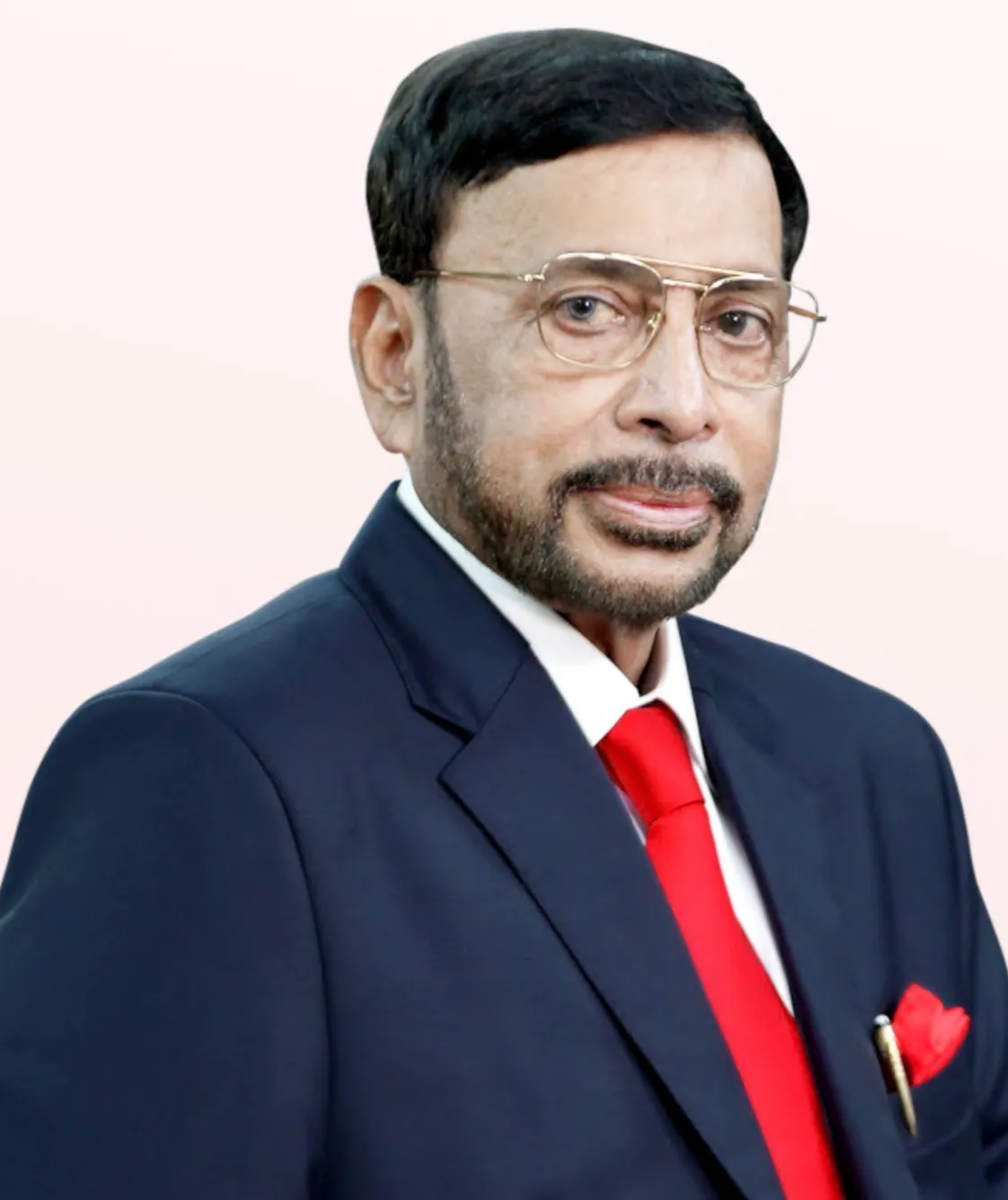 Portrait of a man with glasses and a beard wearing a navy suit, white shirt, and red tie with matching pocket square.