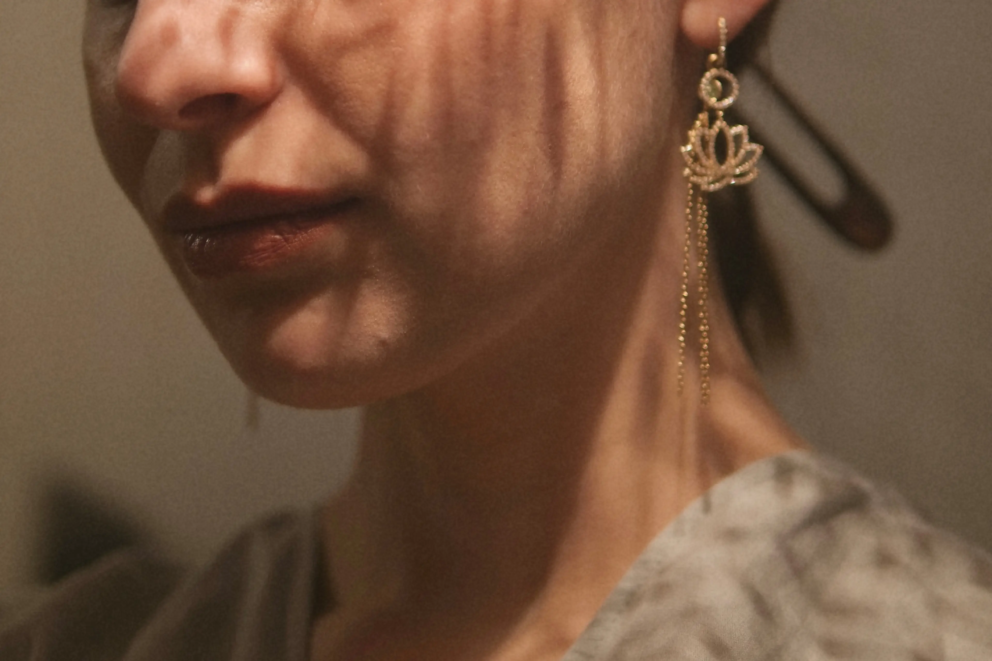 Close-up of a woman’s lower face and neck wearing a gold lotus-shaped dangling earring.