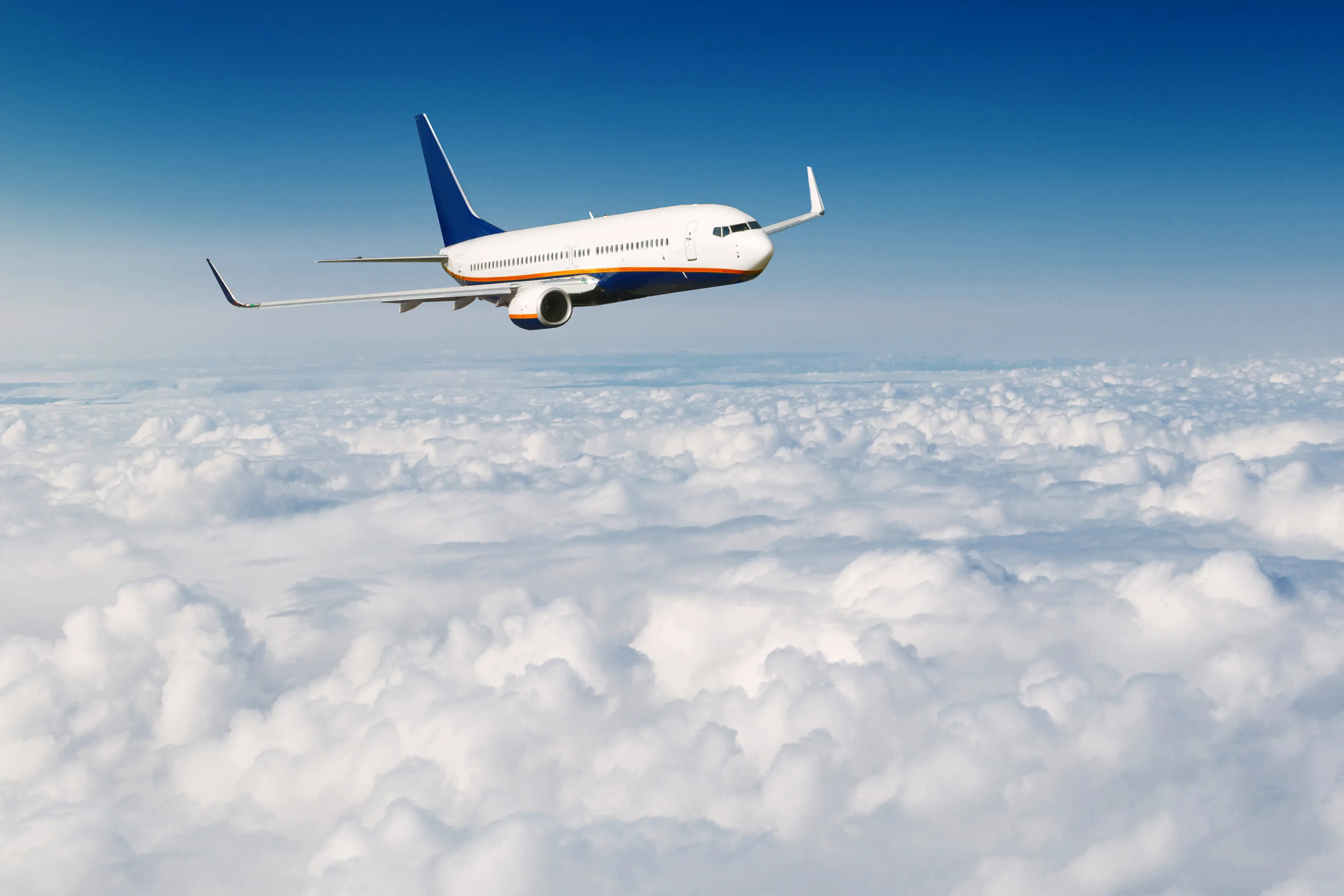 Commercial airplane flying above a dense layer of white clouds under a clear blue sky.