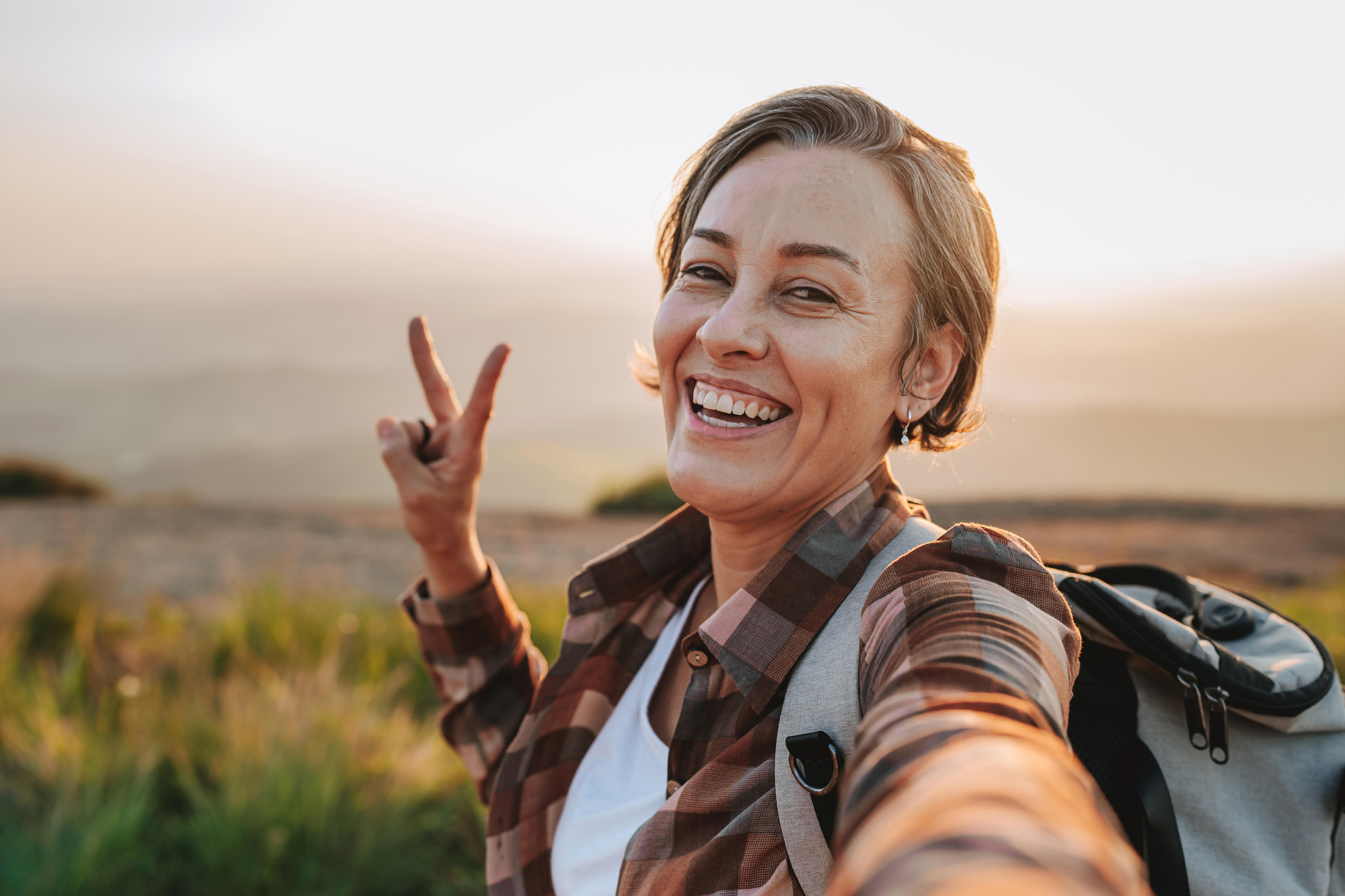 Smiling woman outdoors at sunset making a peace sign