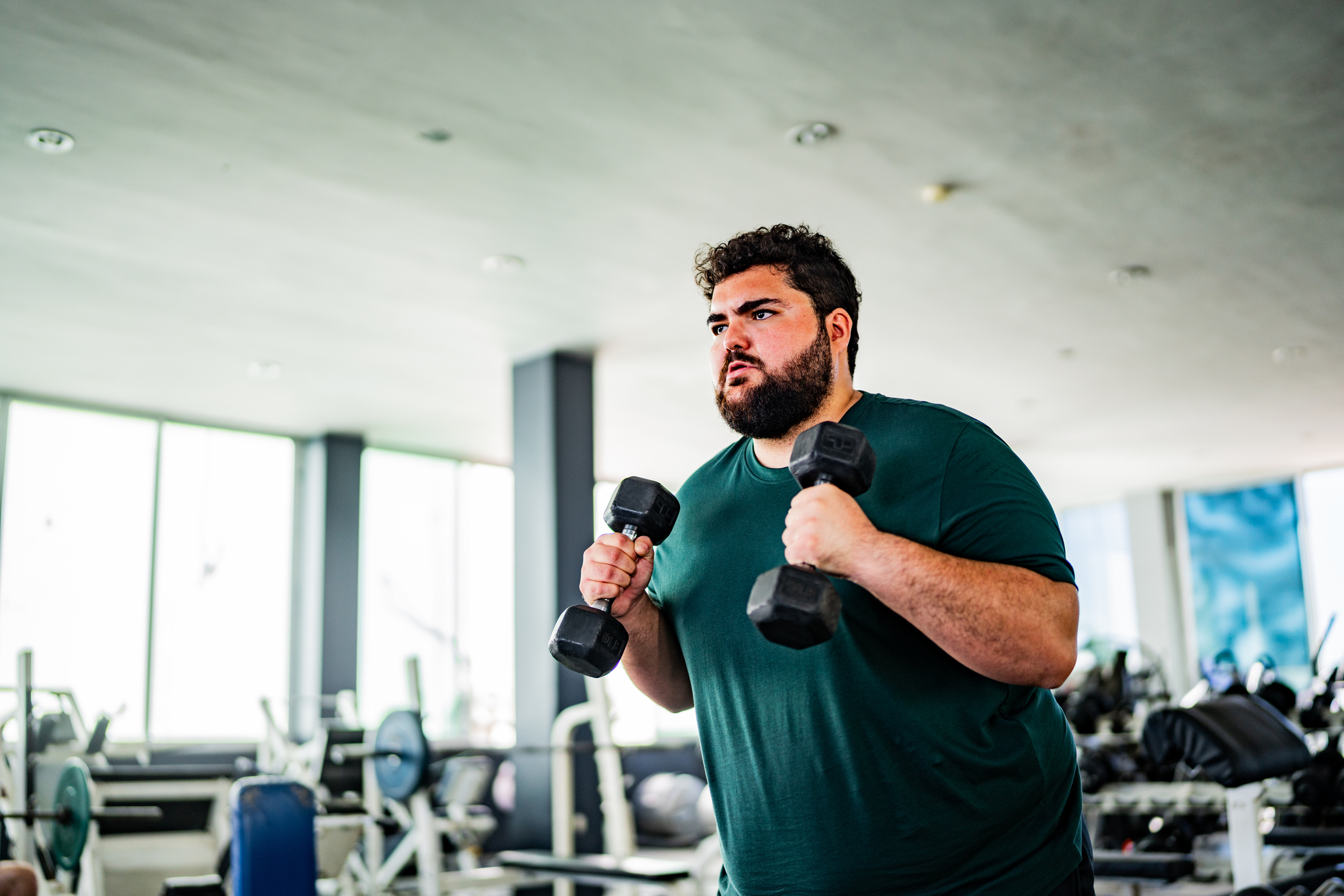Mid adult man doing exercises using dumbbell at gym