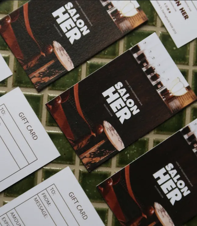 Multiple Salon Her gift cards arranged on a green tiled surface, showing both front and back sides.