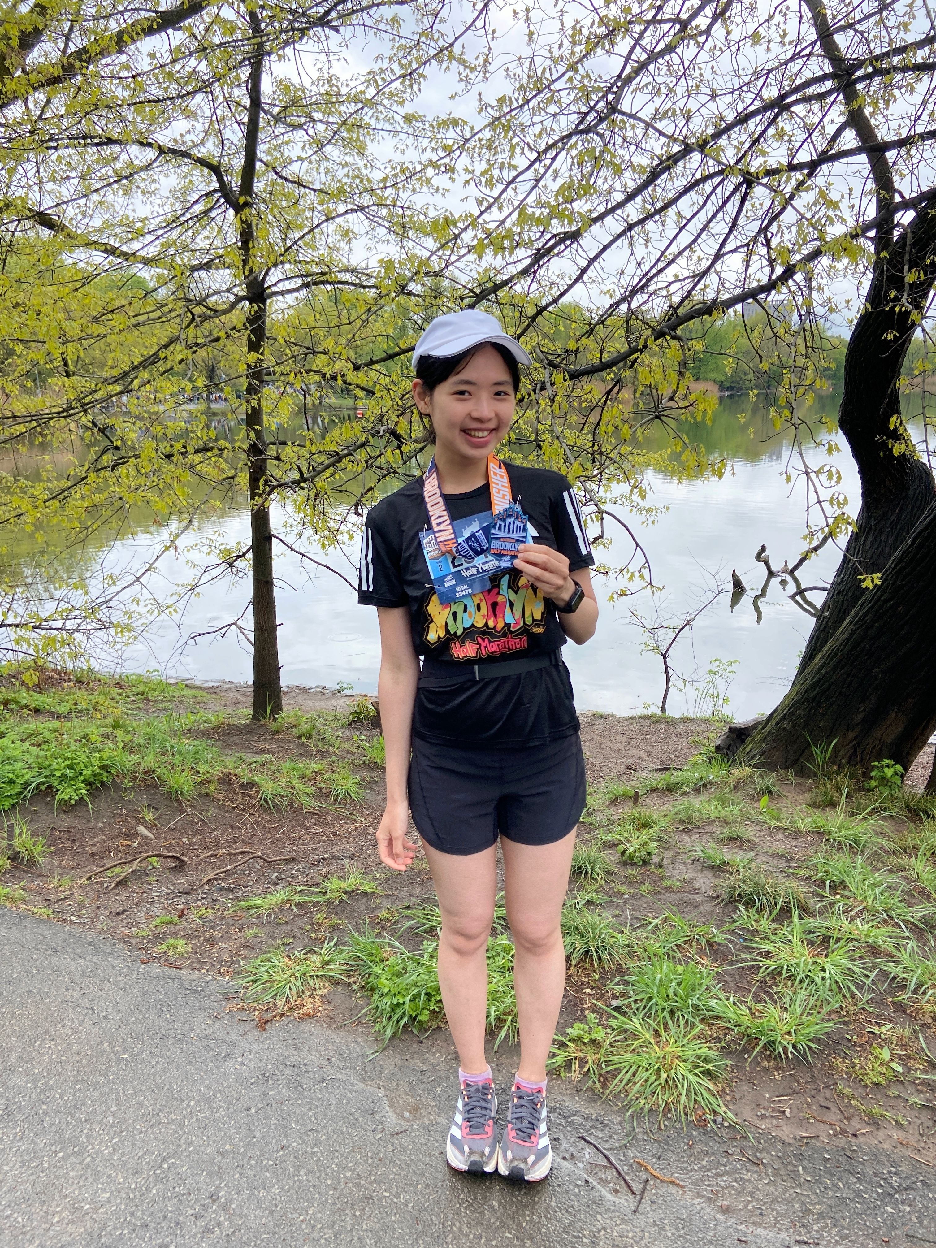 Jessie holding up her Brooklyn Half Marathon finisher medal beside a lake in Prospect Park
