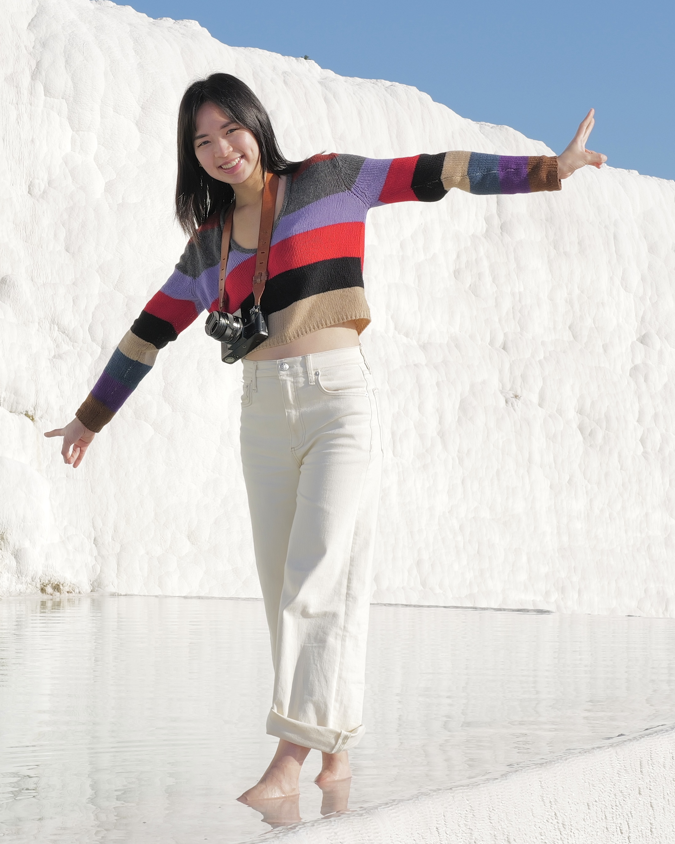 Jessie in a striped sweater, arms out, standing in the shallow water of the white travertine terraces at Pamukkale