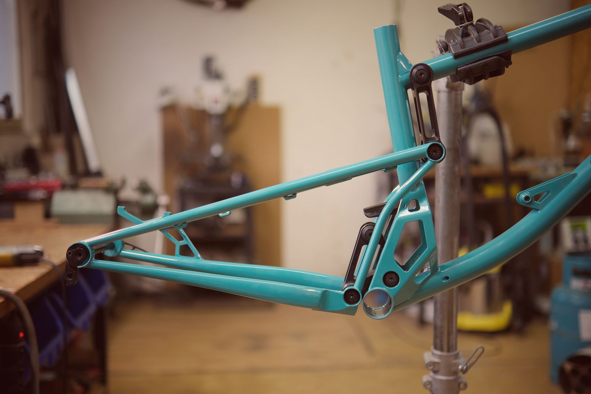 Close-up of a teal bicycle frame mounted on a repair stand in a workshop.