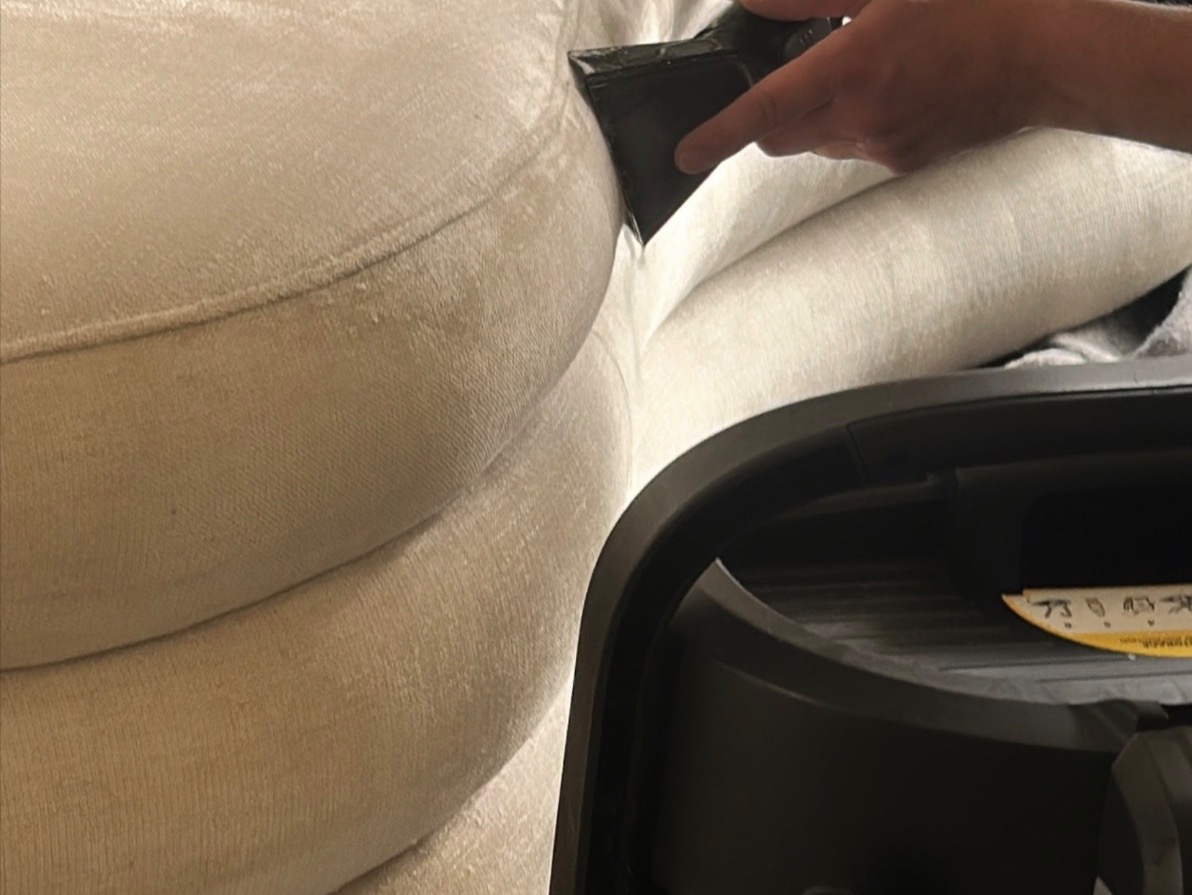Gros plan d’un technicien nettoyant en profondeur un canapé en tissu beige avec un aspirateur professionnel.