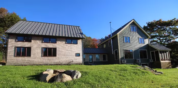 Two modern houses with metal roofs on grassy lawn with large rocks