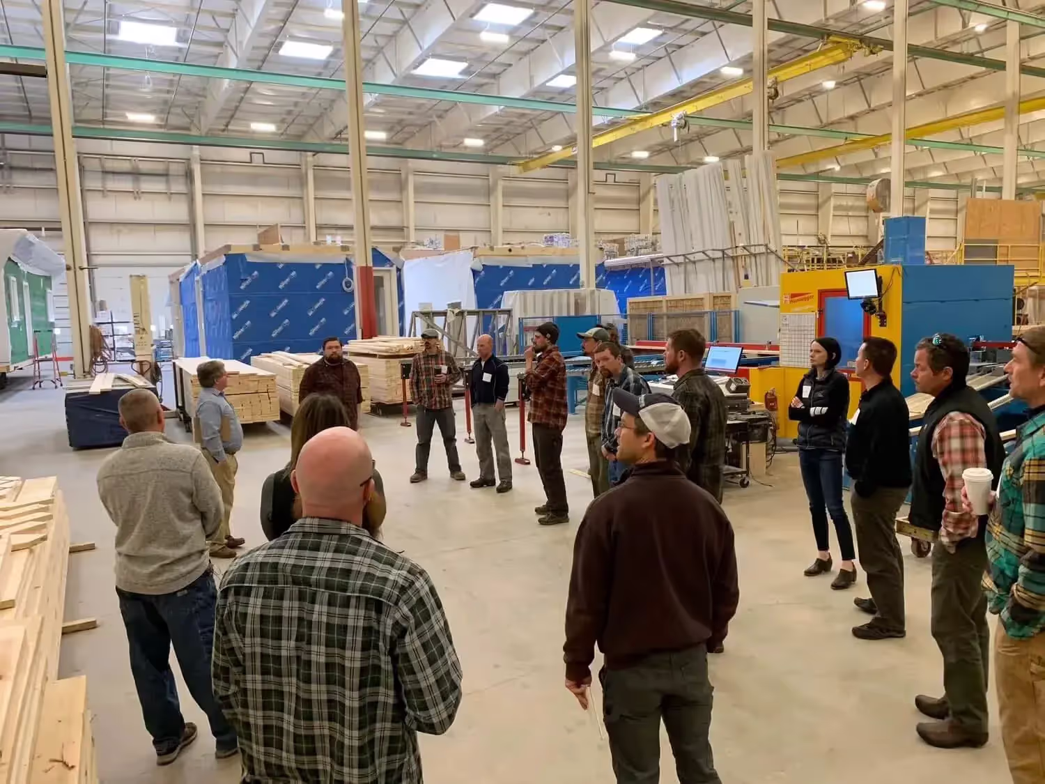 Workers gather for meeting in industrial warehouse with lumber and machinery