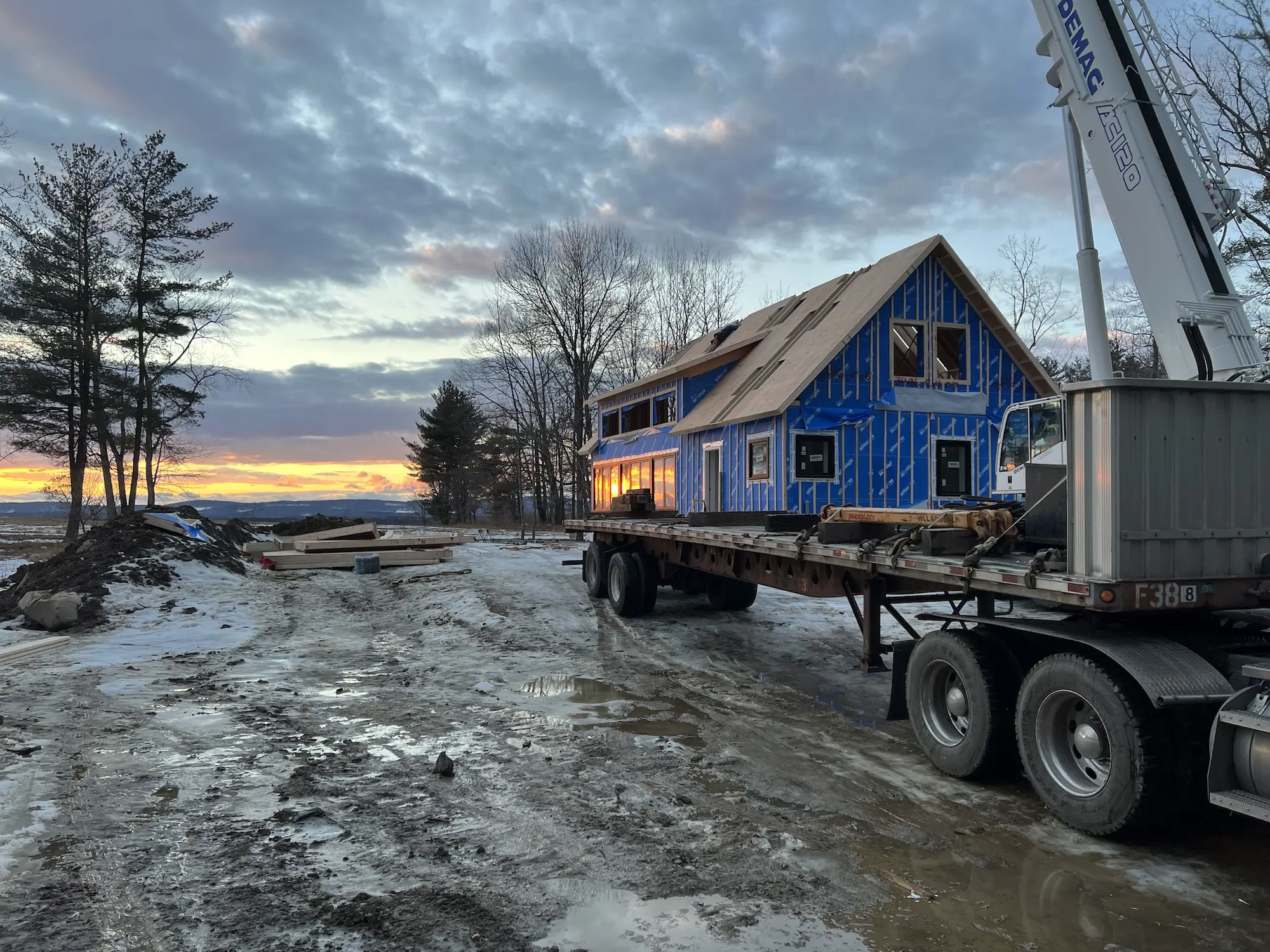 Blue house on flatbed truck at construction site during winter sunset