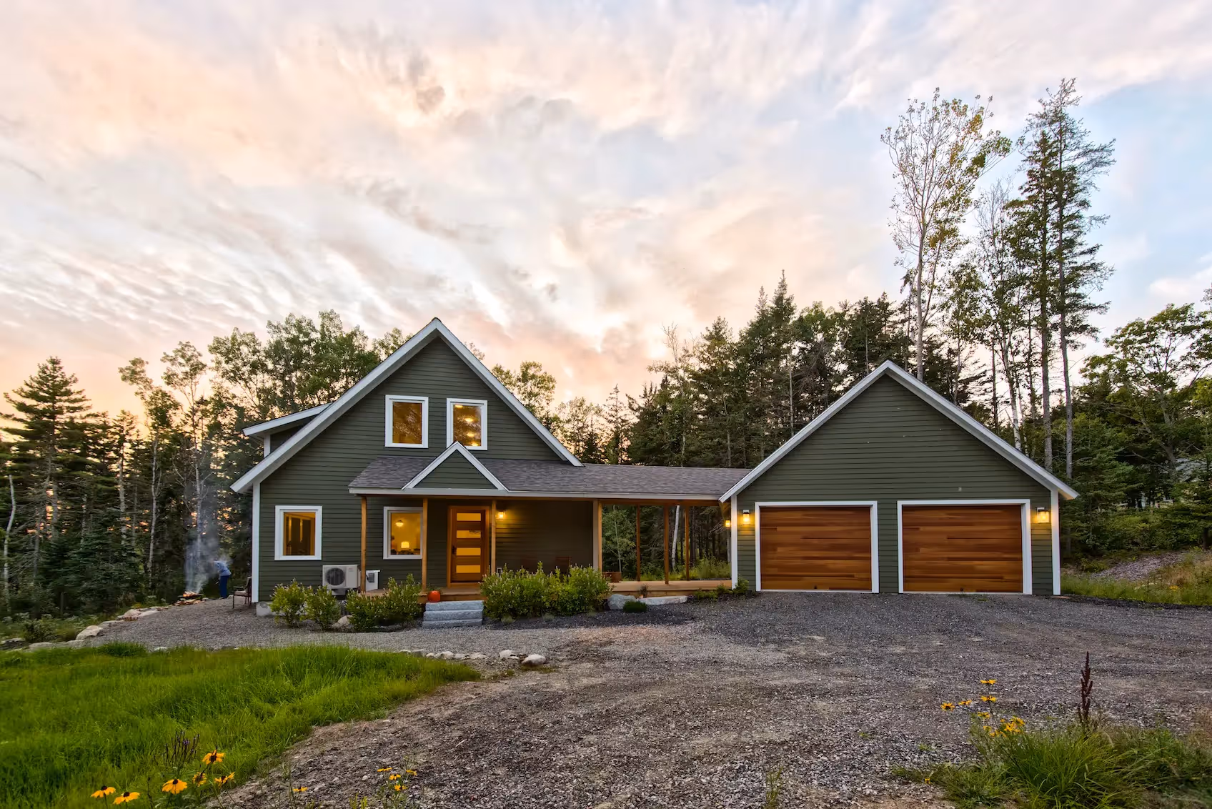 Green wooden house with two-car garage in forested area at sunset