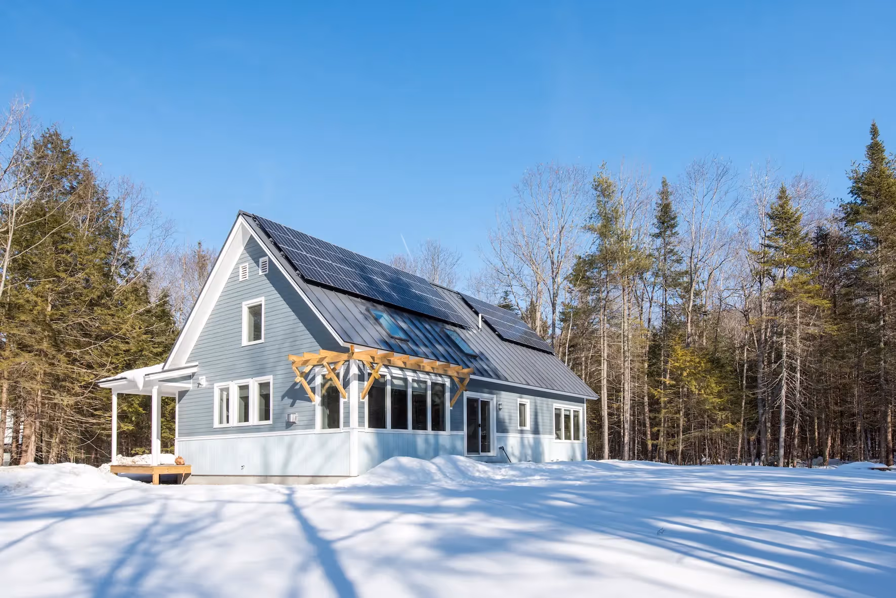 Solar-powered blue house in snowy forest with wooden porch
