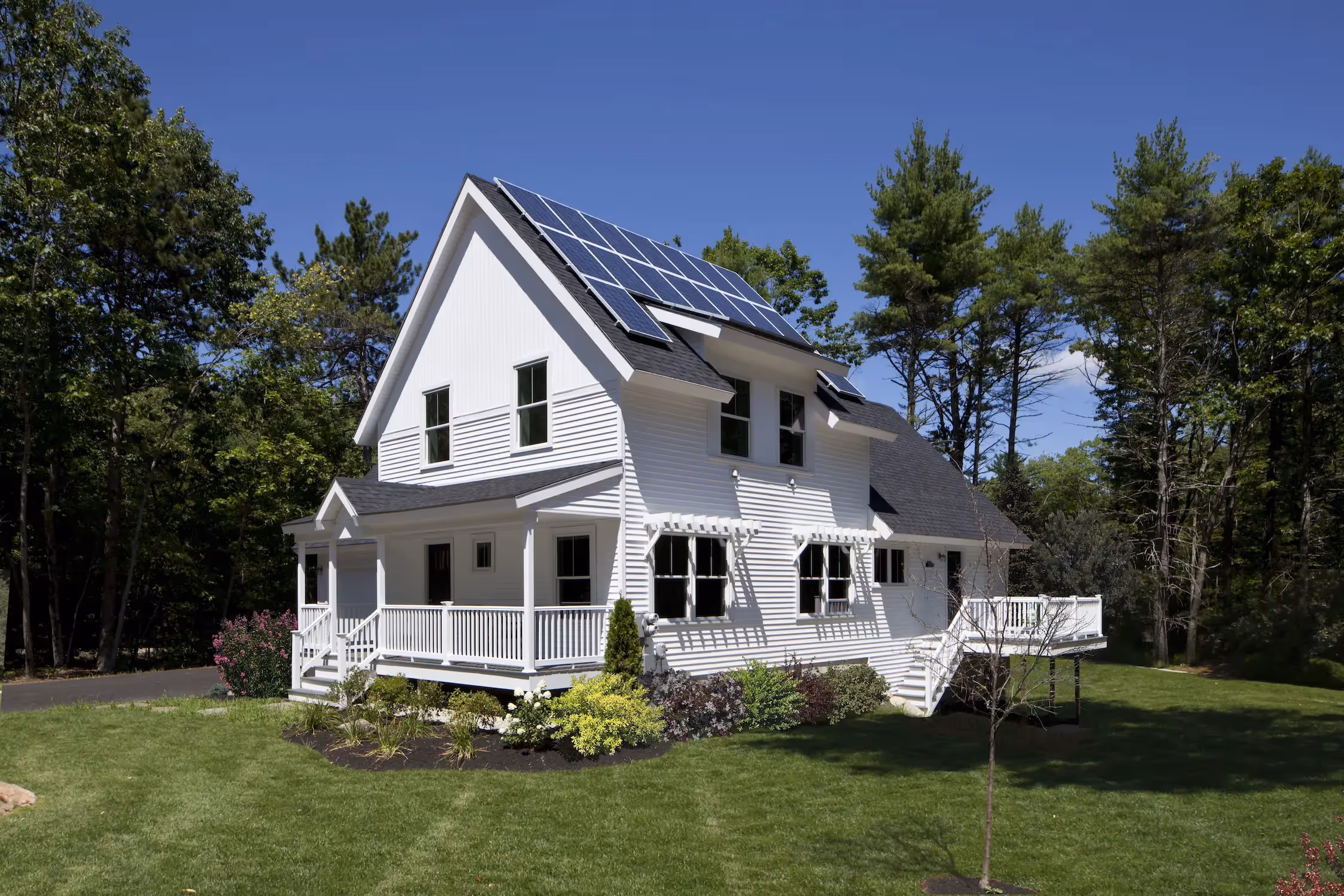 White two-story house with solar panels surrounded by trees and green lawn
