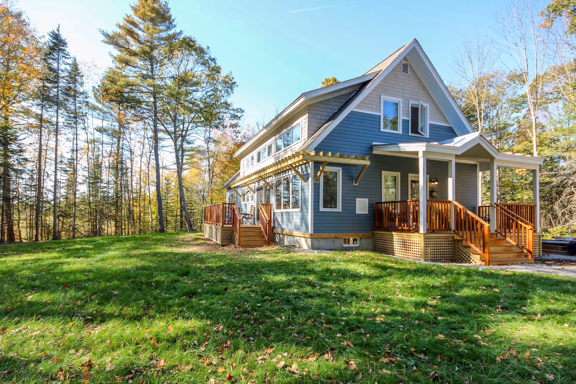 Blue cottage with wooden deck nestled in autumn forest with green lawn
