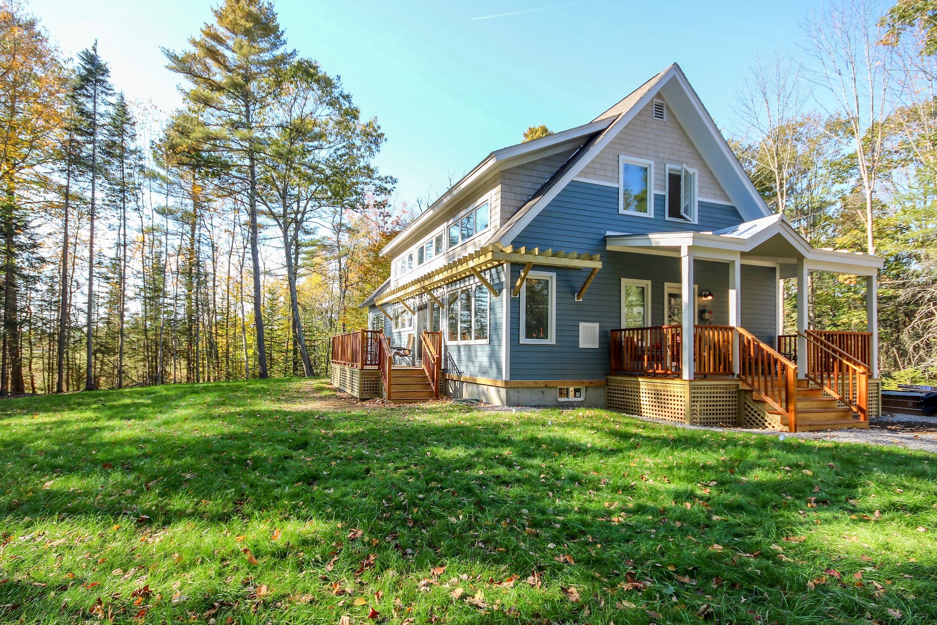 Blue cottage with wooden deck nestled in autumn forest with green lawn