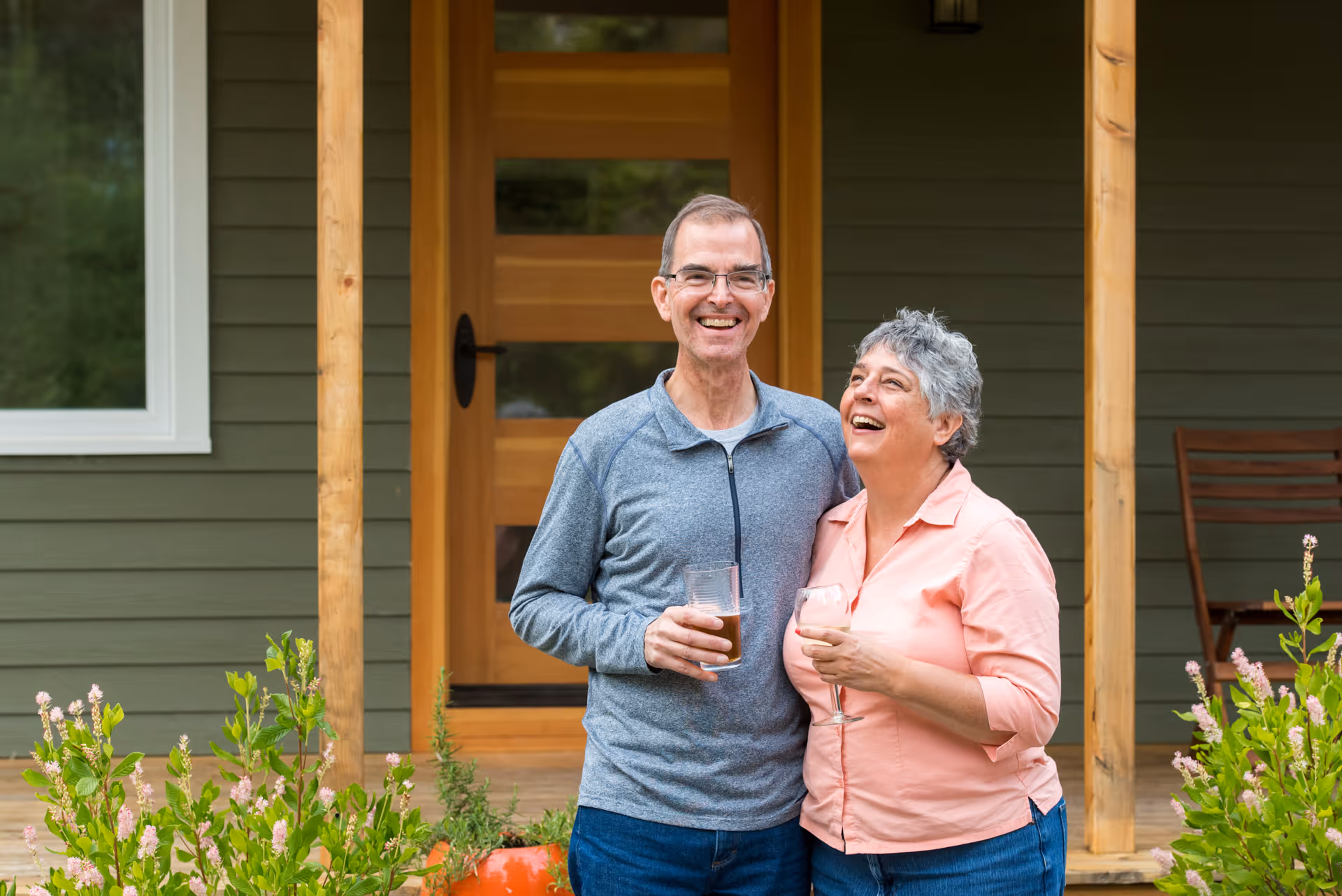Smiling mature couple enjoying drinks on home porch with flowering plants
