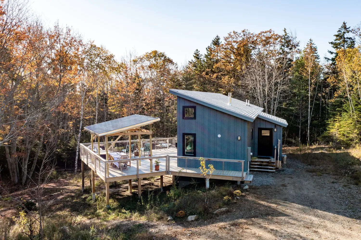 Blue tiny house with deck in autumn forest surrounded by trees
