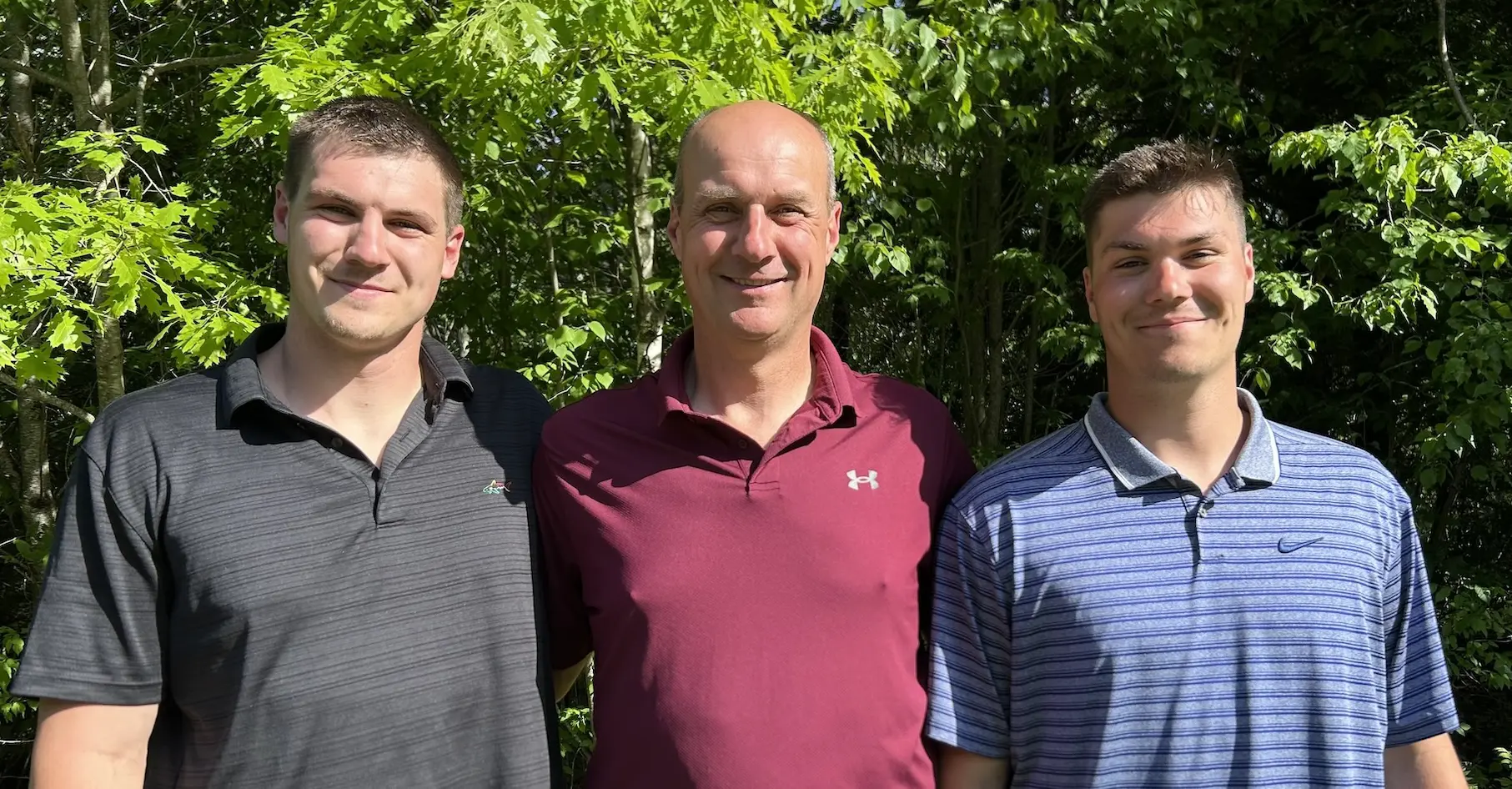 Three men posing together outdoors with green trees in background
