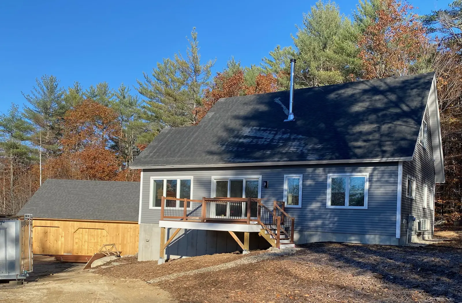 Blue house with wooden deck in autumn forest with pine trees